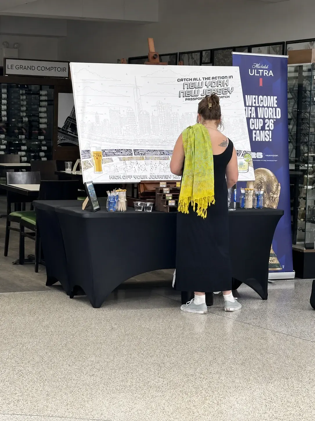 Guest painting a New York New Jersey World Cup paint-by-number mural beside a Michelob ULTRA banner at JFK