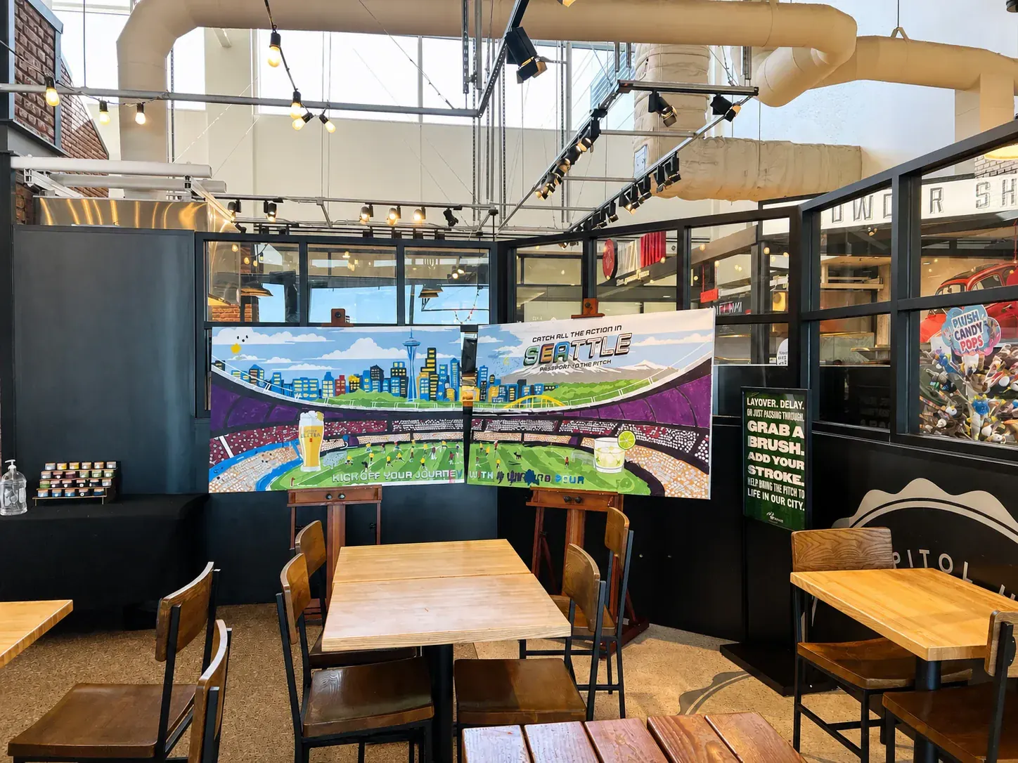 Completed two-panel Seattle World Cup paint-by-number mural displayed on easels in the airport event space