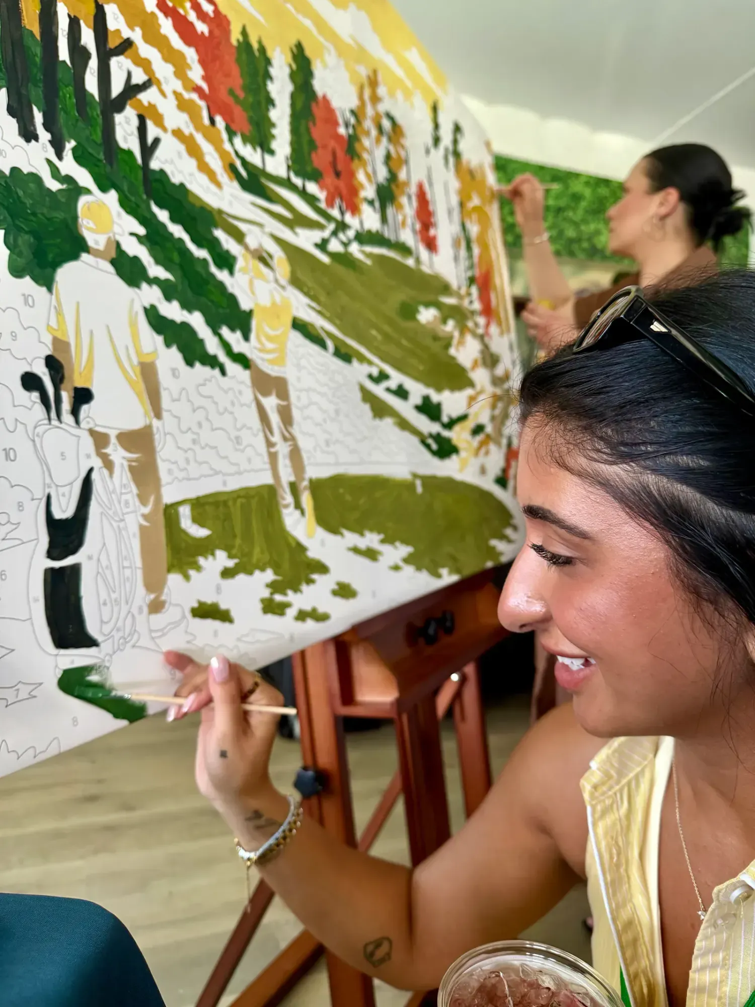 Guest adding green paint to a numbered golf scene on a paint-by-number mural