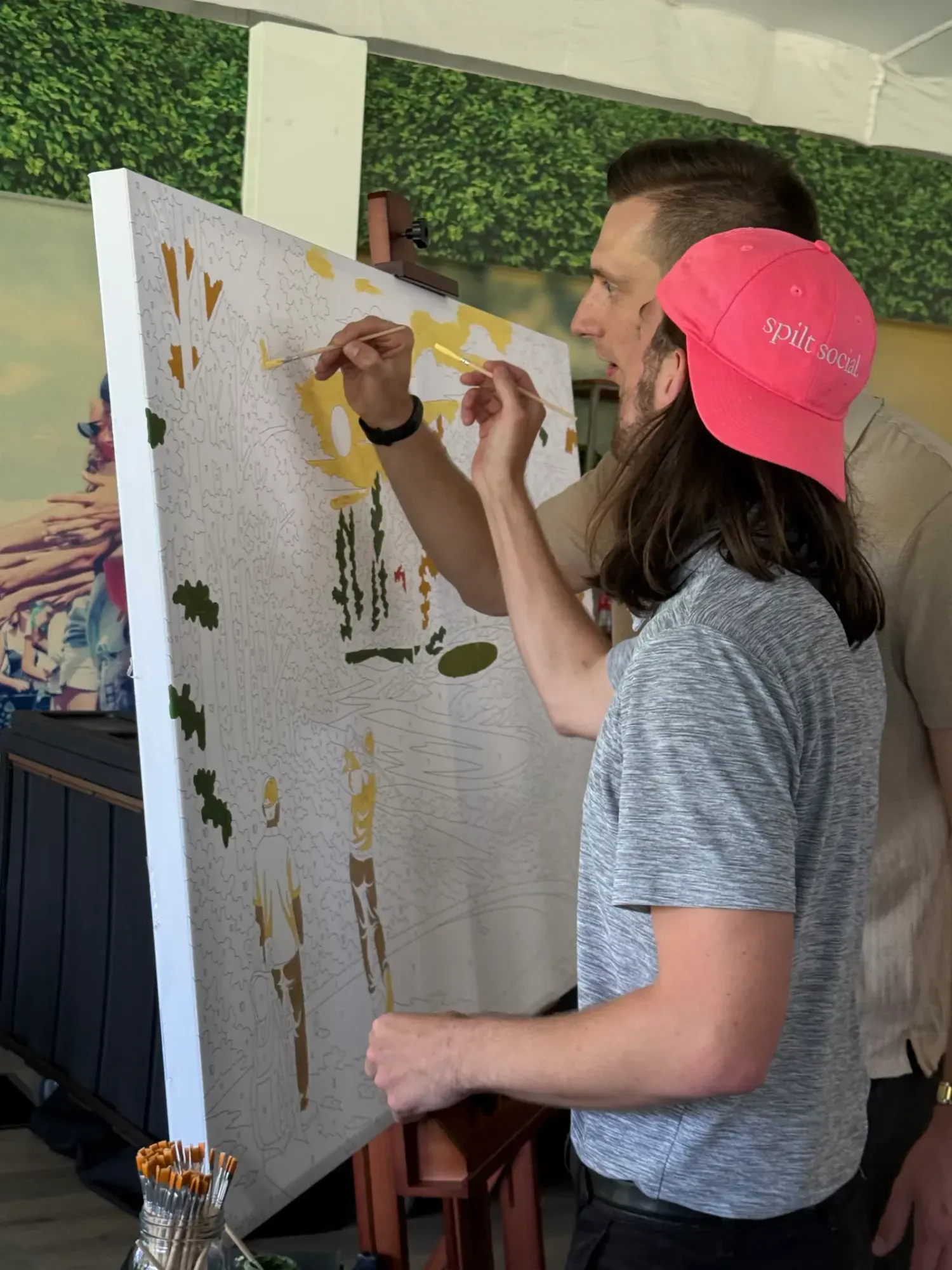 Attendee painting a golf-themed paint-by-number mural beside its wooden easel and paint supplies