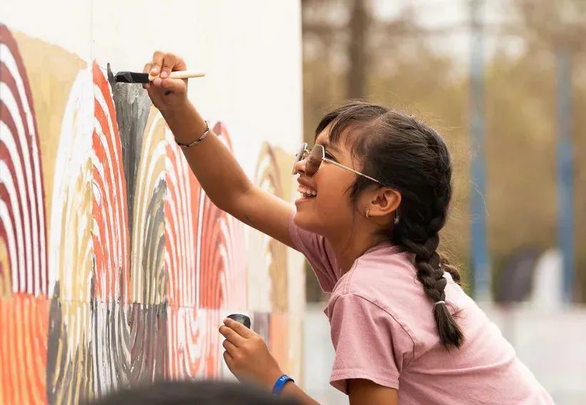 Young guest wearing sunglasses painting numbered sections of a large collaborative paint-by-number mural