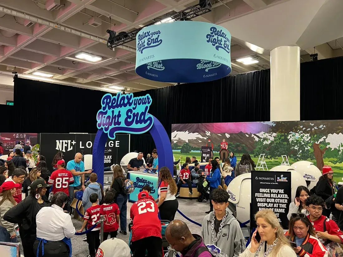 Crowded Novartis Relax Your Tight End booth with fans, relaxation pods, and a collaborative paint-by-number mural